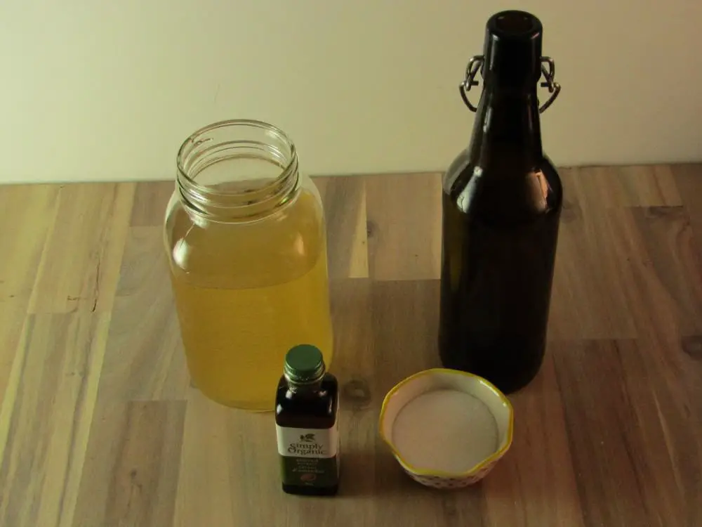 a bottle of almond extract with a bowl of sugar with a mason jar of kombucha and an empty swing top bottle