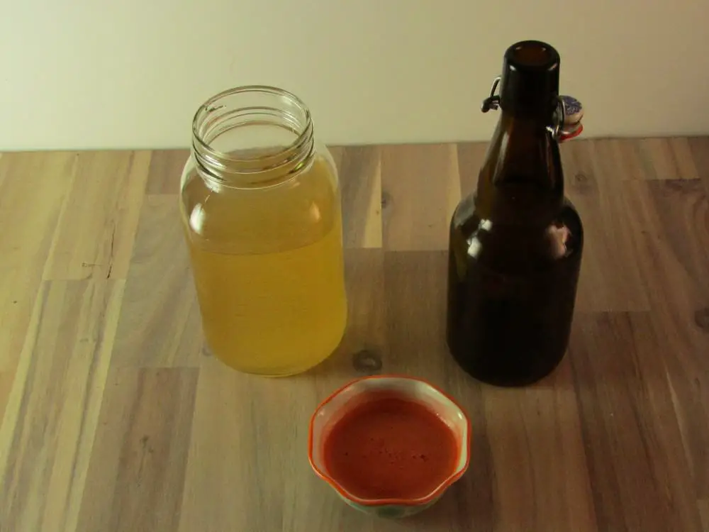 Bowl of freshl carrot juice with a mason jar of kombucha and an empty swing top bottle