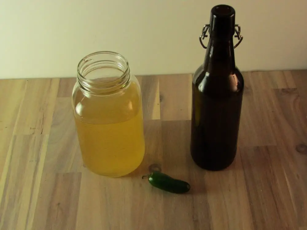 A jalapeno pepper with a mason jar of kombucha and an empty swing top bottle 