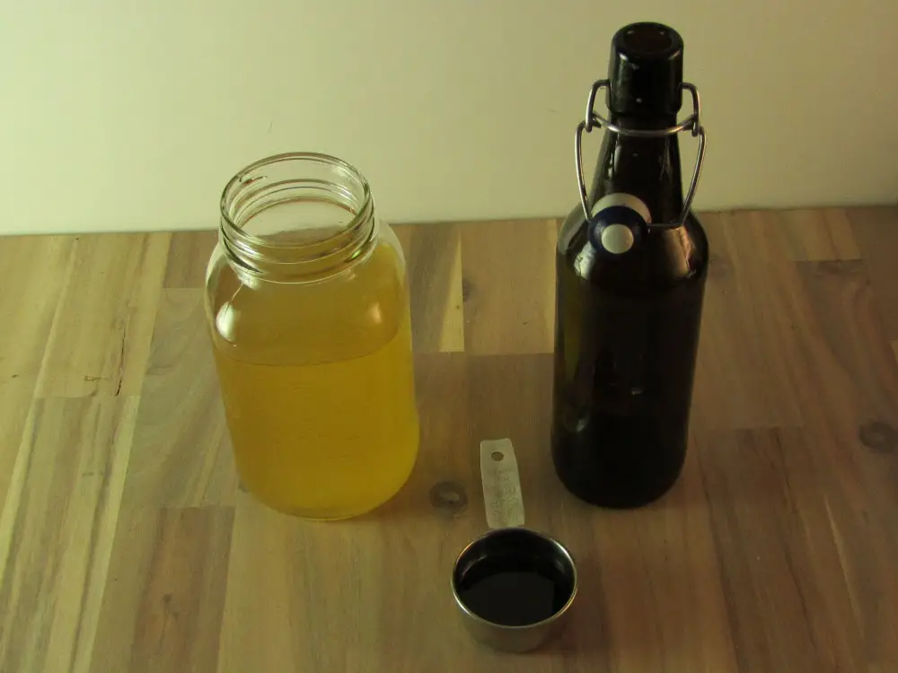1/4 cup measure of molassis with a mason jar of kombucha and an empty swing top bottle