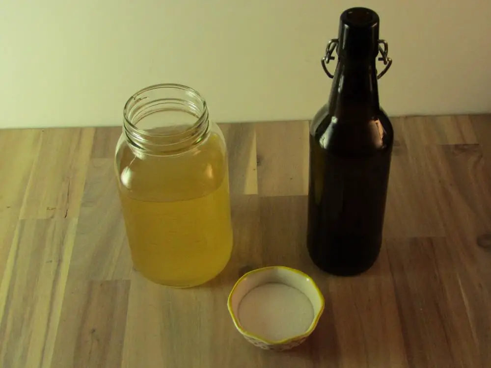 Bowl of sugar with a mason jar of kombucha and an empty swing top bottle