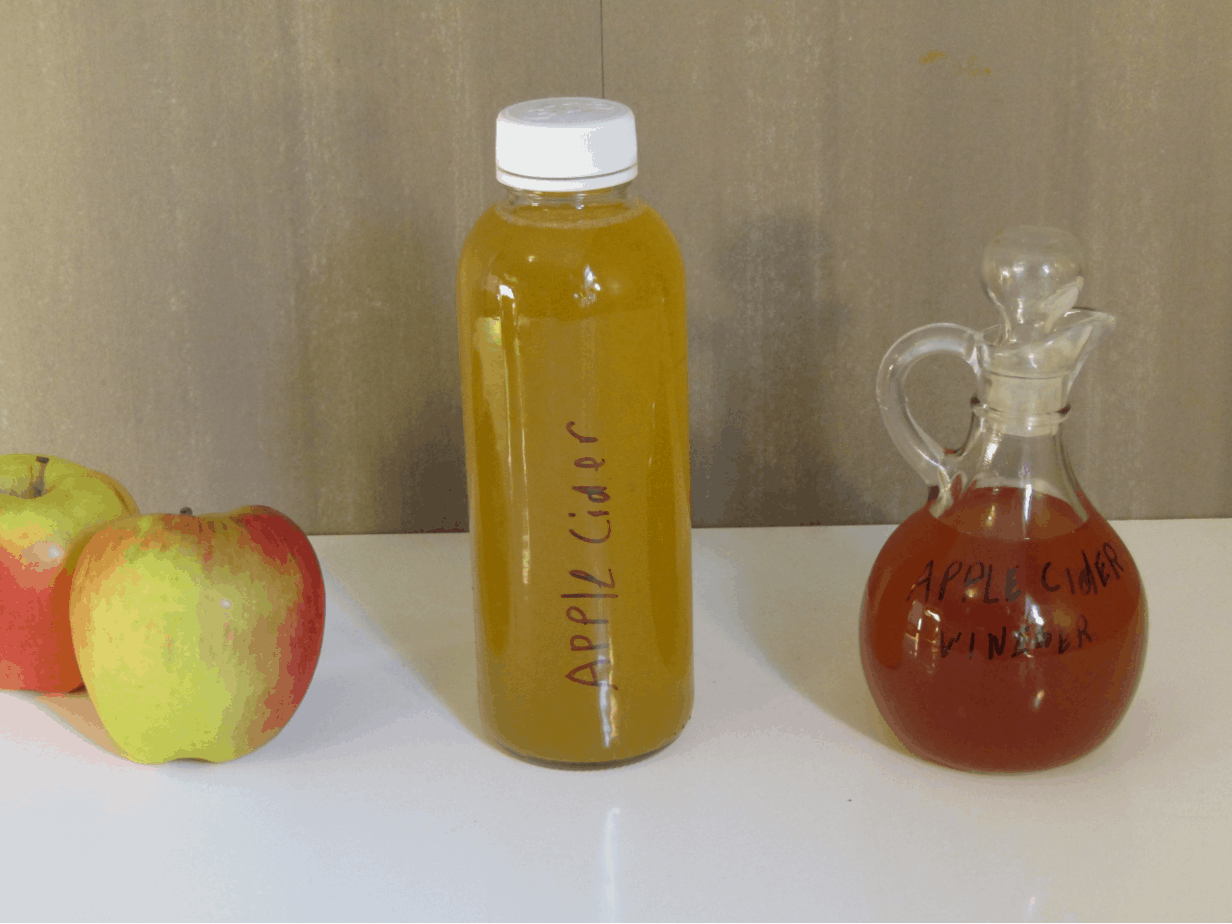 Two apples a bottle of apple cider and a bottle of apple cider vinegar