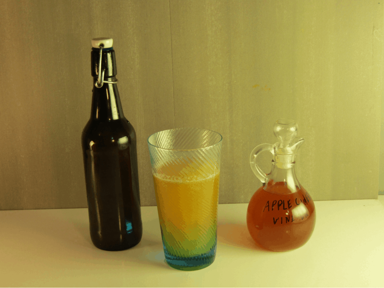 A bottle of kombucha, glass of kombucha and a contaner of apple cider vinegar
