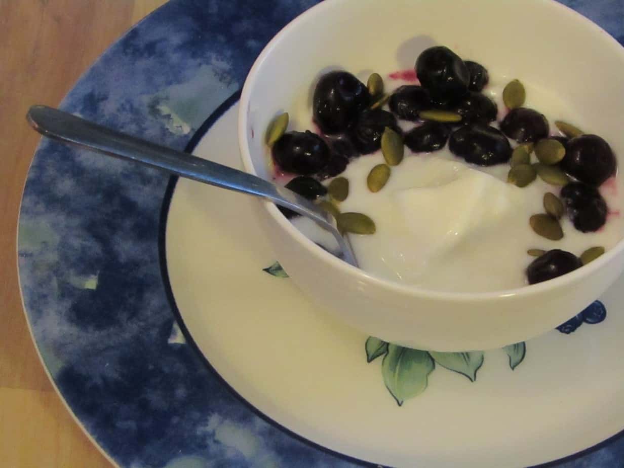 Bowl of yogurt with some blueberries and pumpkkin seeds on a plate with a spoon