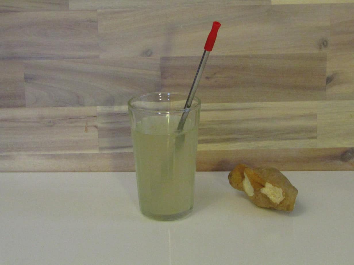Glass of ginger ale with a straw and a piece of fresh ginger