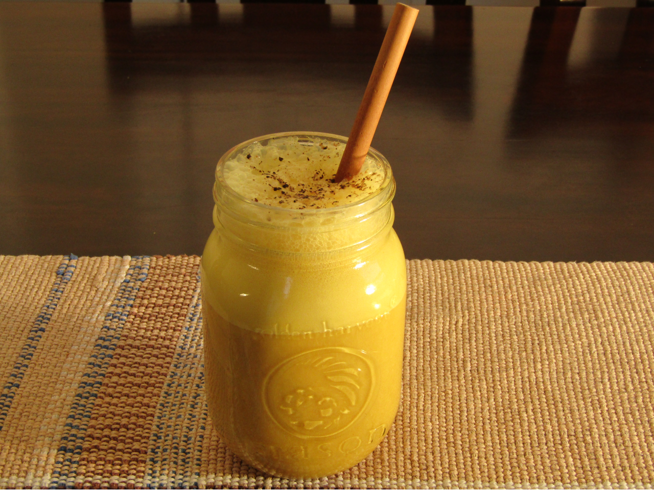 Mason Jar on a table filled with ginger tumeric tonic with a straw