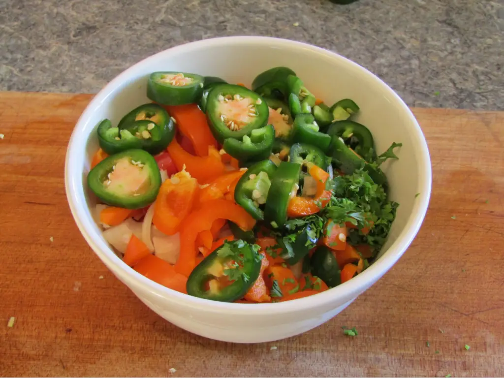 Salsa ingredients: tomatos, garlic, onion, peppers and parsly in a bowl on a cutting board