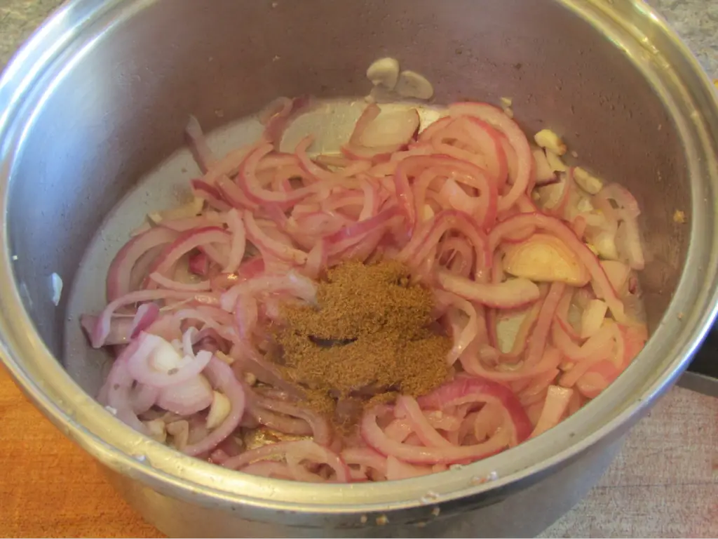 cooked onion and garlic in pot with added cumin on top