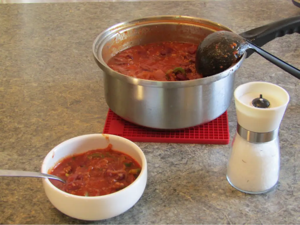 bowl of chili, a salt grinder with a pot of chili in background
