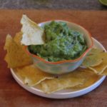 bowl of guacamole on a plate filled with corn chips