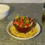 Bowl of fresh salsa made with fermented hot peppers on a plate with corn chips around the outside.