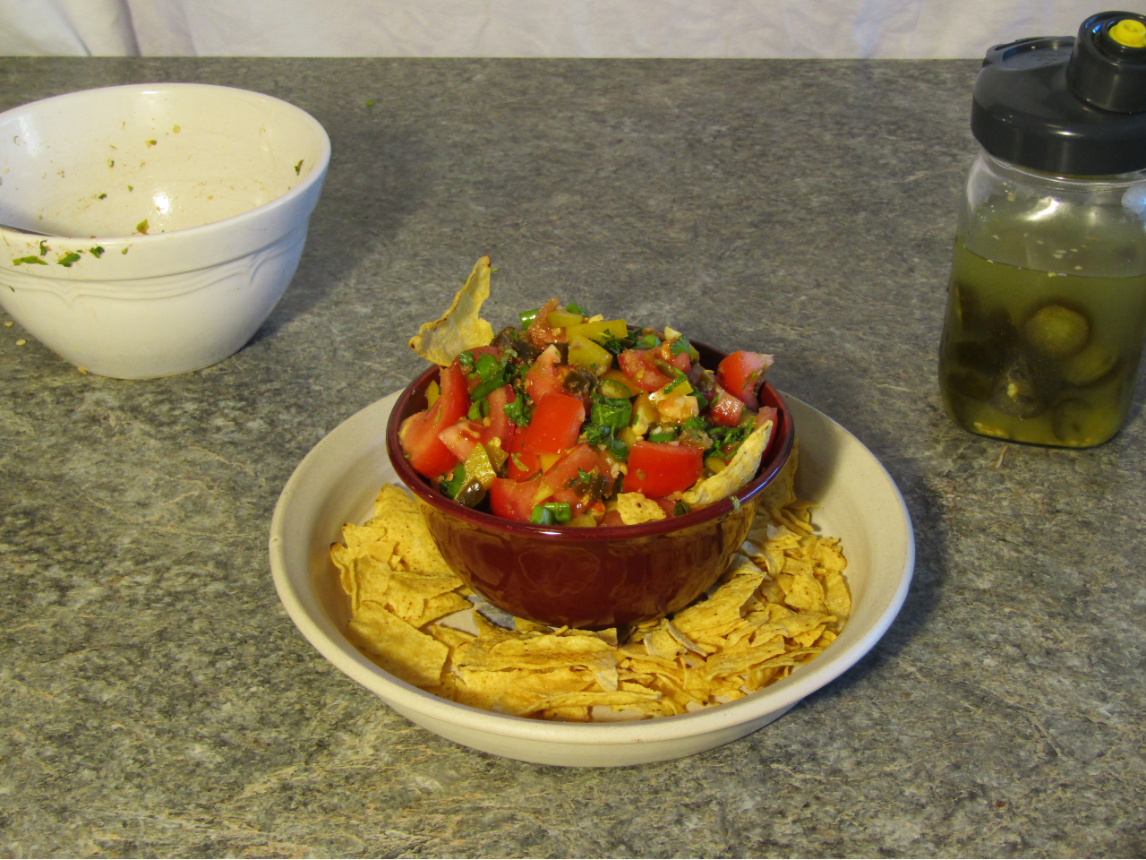 Bowl of fresh salsa made with fermented hot peppers on a plate with corn chips around the outside.