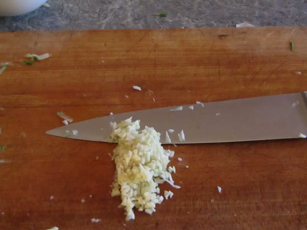 Minced garlic and a knife in the background on a cutting board