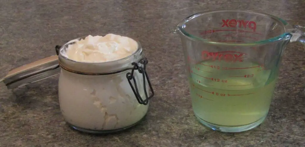 A swing topped jar filled with greek yogurt sitting beside a measuring cup with whey in it.