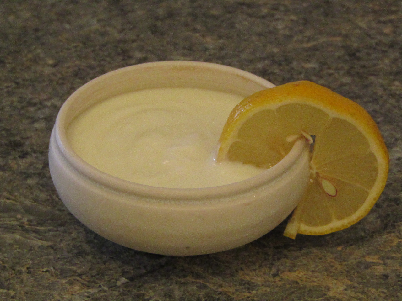 Bowl of yogurt with a slice of lemon hanging on the side